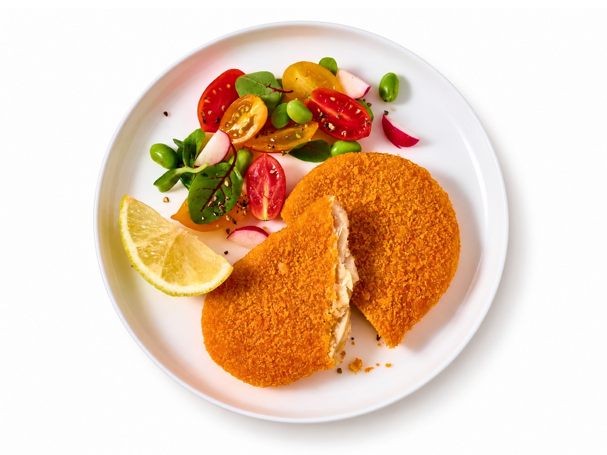 Plant-based schnitzel cut open on a plate with salad and lemon