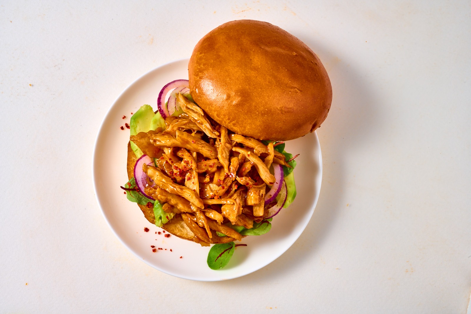 Plant-based seasoned strips in a bun with avocado and red onion on a white plate